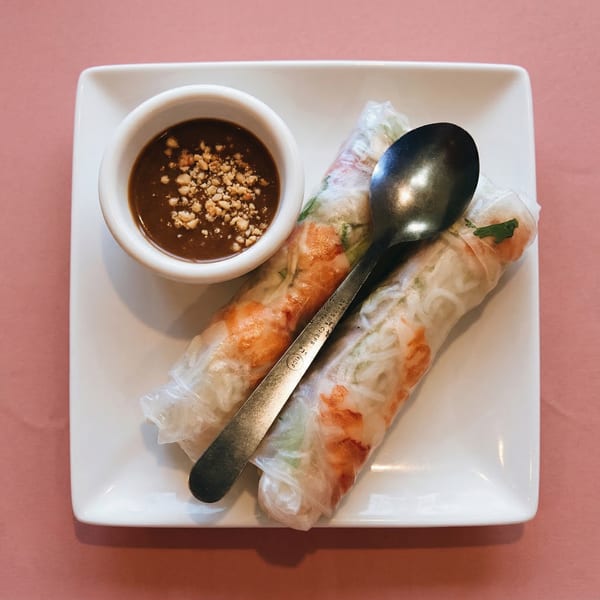Two Vietnamese spring rolls with shrimp and herbs, served with peanut sauce and a spoon.