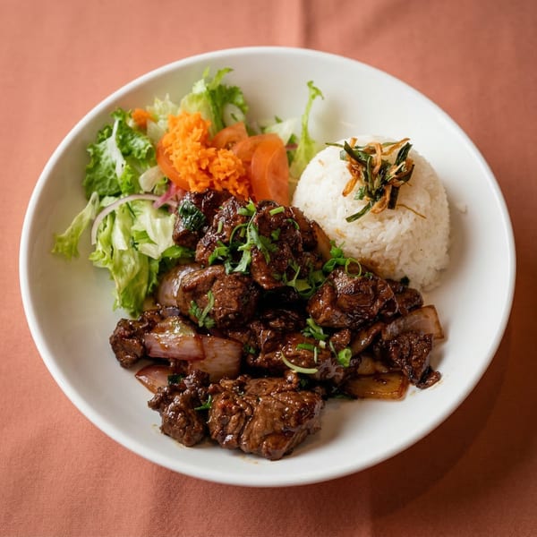 Miss Saigon Cafe's Vietnamese shaking beef with rice, salad, and pickled carrots in a white bowl.