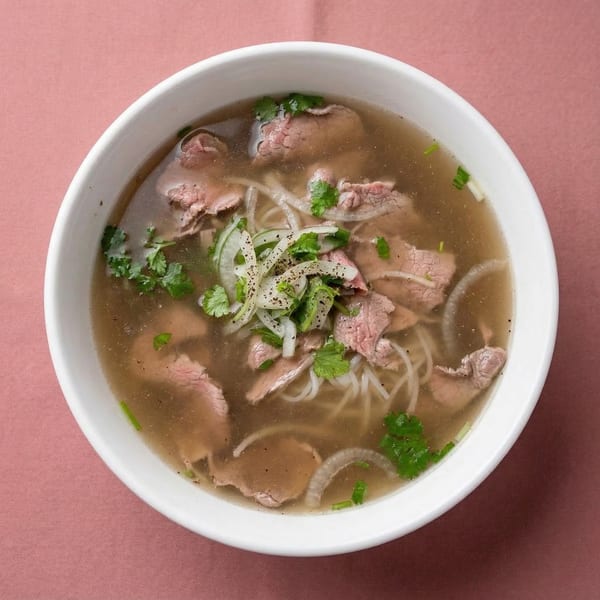A bowl of Miss Saigon Cafe's Vietnamese pho with beef, noodles, onions, and cilantro.