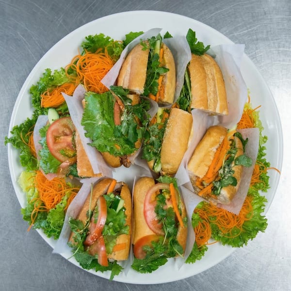 A large white platter filled with several Vietnamese banh mi sandwiches, garnished with lettuce and shredded carrots.