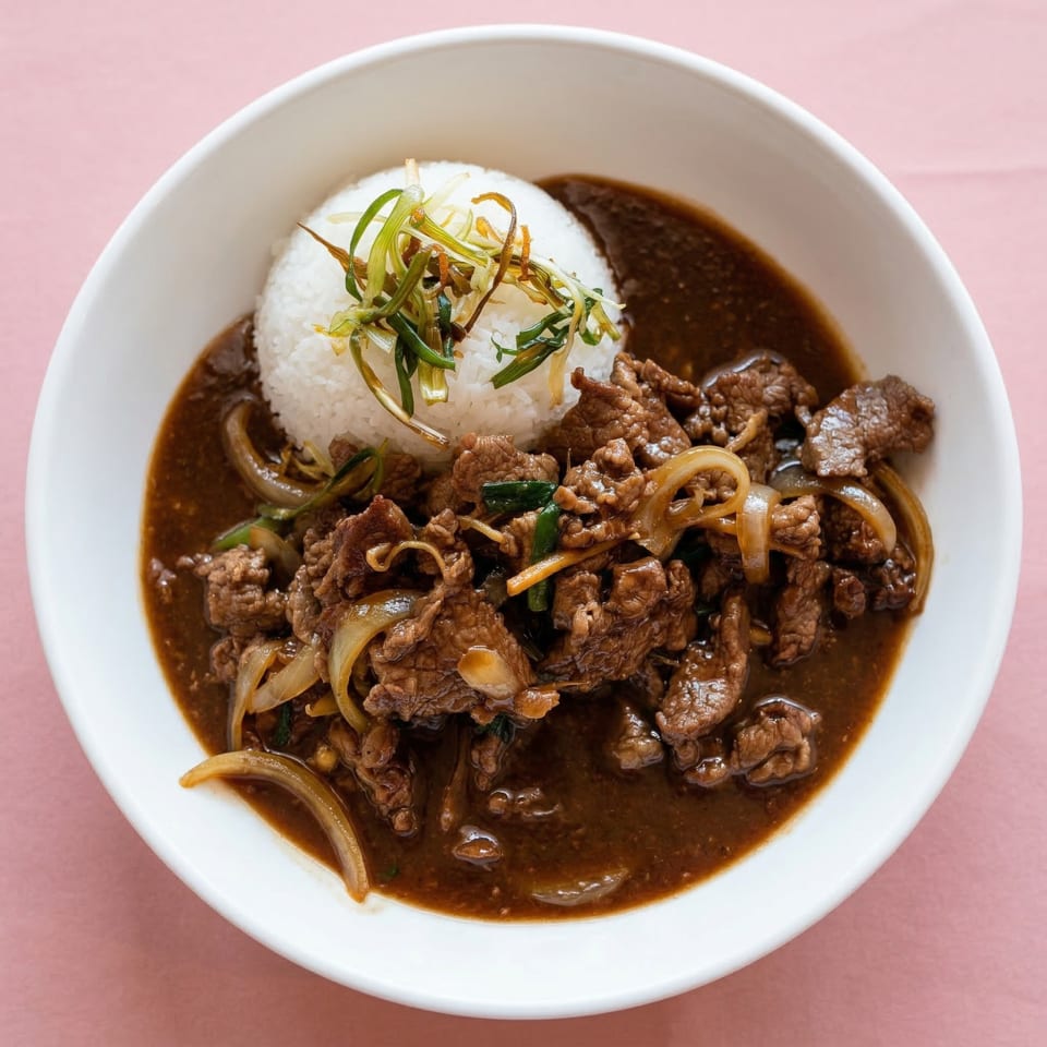 Vietnamese beef stir-fry with onions and a side of white rice, garnished with green onions.